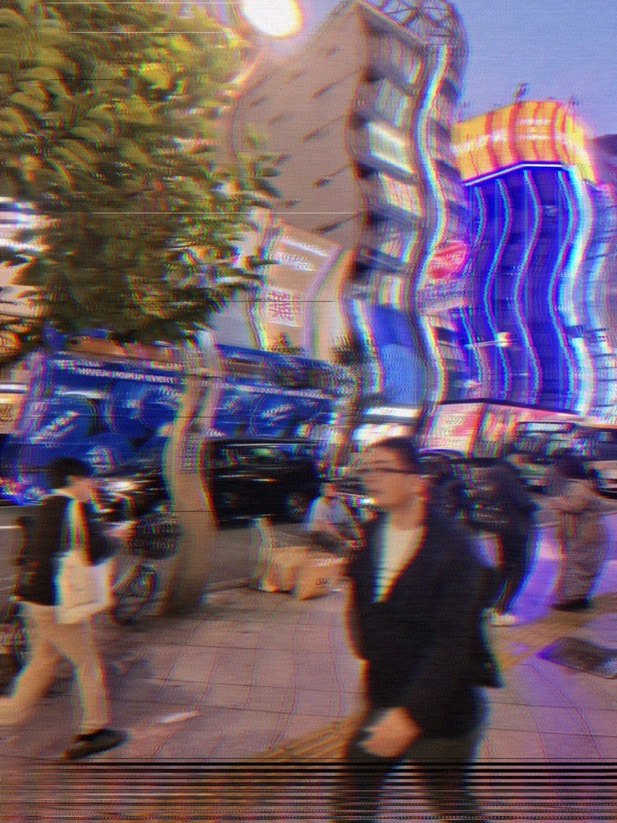 The same street through VHS: colour bleeding sideways off the neon, tracking tear across the lower frame, everything softened like a worn tape.