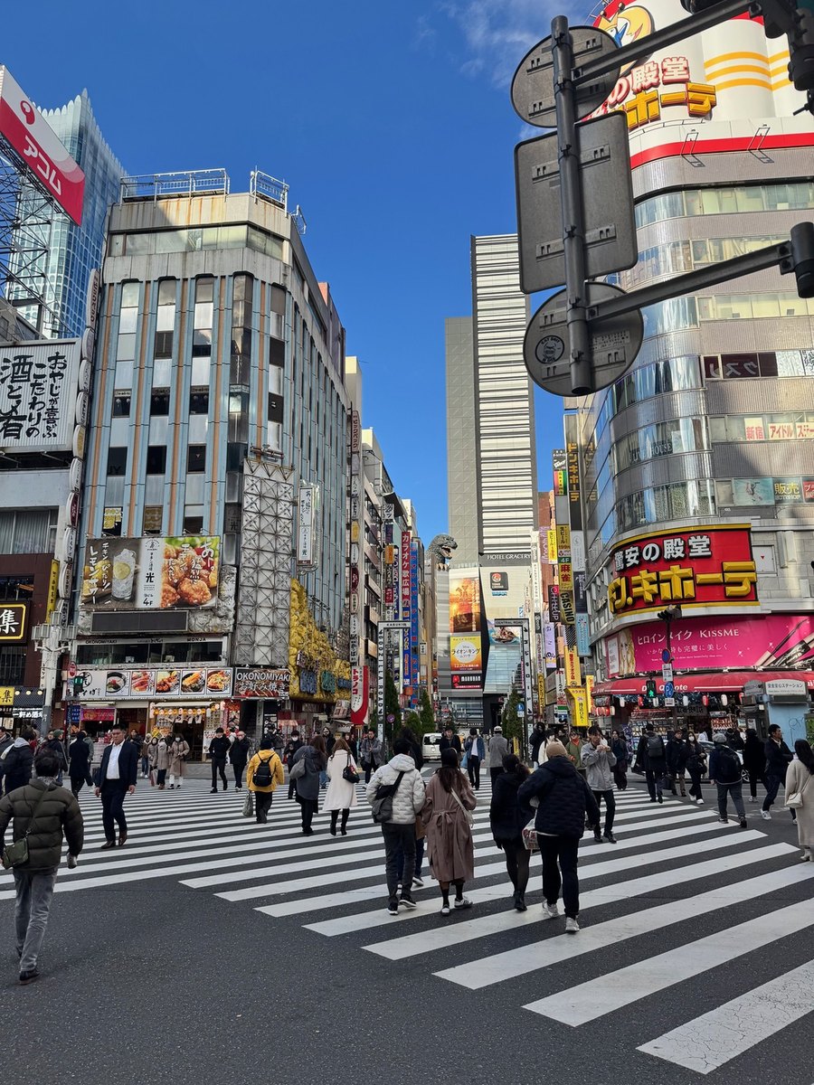 The original photograph of a Tokyo crossing on a clear day: office towers, signage, a crowd on the striped crossing.